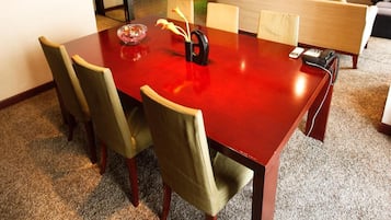 Un salón de conferencias con una mesa roja, sillas verdes, un jarrón con flores y un cuadro en la pared.