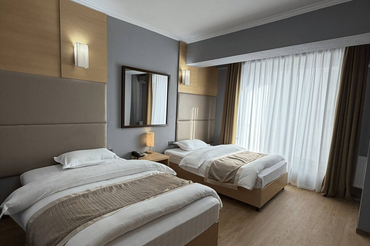 Hotellihuone, jossa on kaksi sänkyä, suuri peili, yöpöytä lampun kanssa ja kattovalaisin.