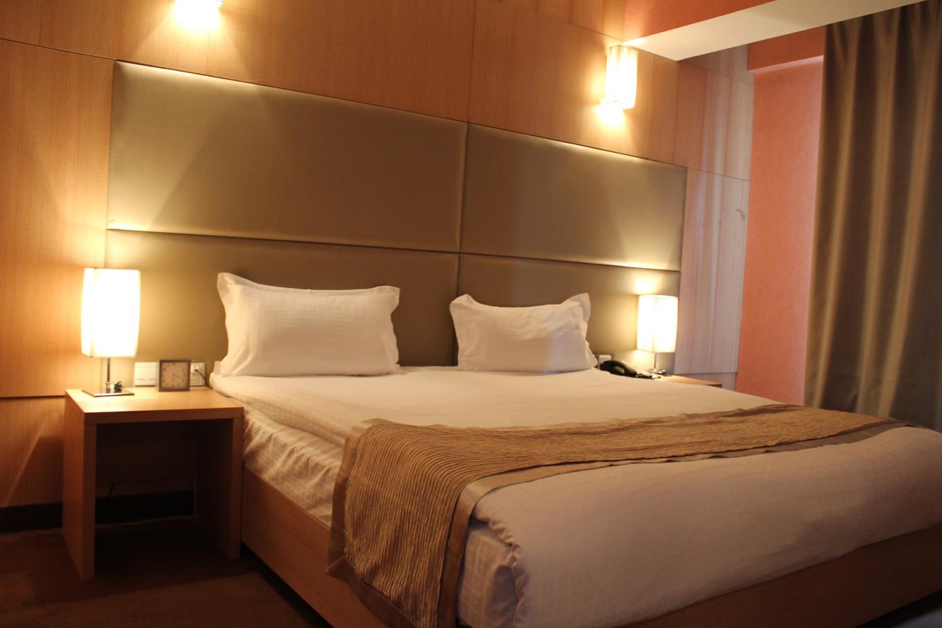 Ein Hotelzimmer mit einem großen Bett, zwei Nachttischlampen, einem Nachttisch und einem Kopfteil mit integrierter Beleuchtung.