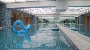 Uma piscina interior ampla com água cristalina, paredes azulejadas e um design moderno no teto.