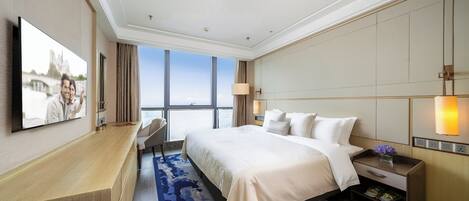 A hotel room with a large bed, a desk, a TV, and a view of the city.
