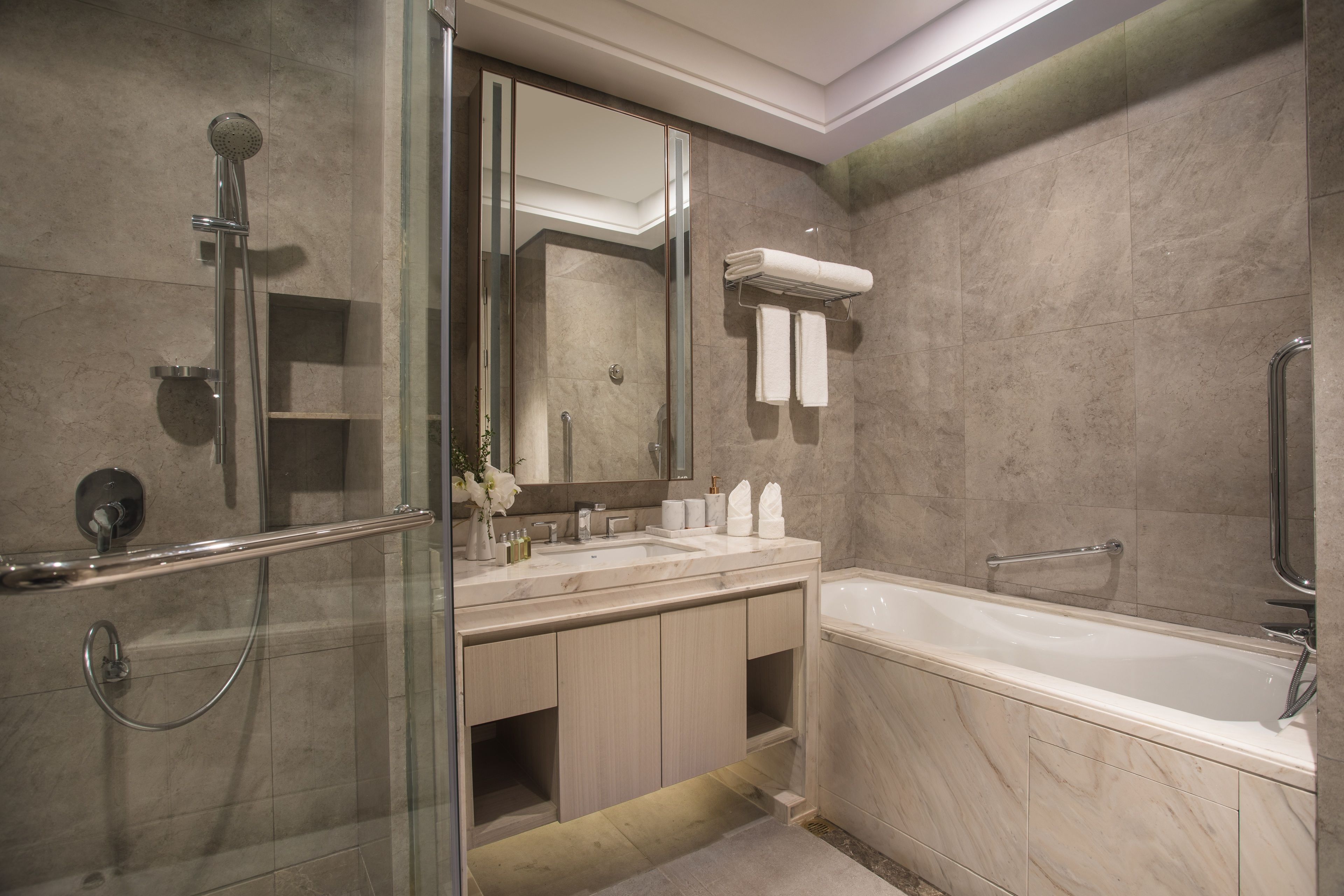Ein modernes Badezimmer mit einer Glaskabine zur Dusche, einem großen Spiegel, einer Badewanne und einem Waschtisch mit Spüle und Handtuchhalter.