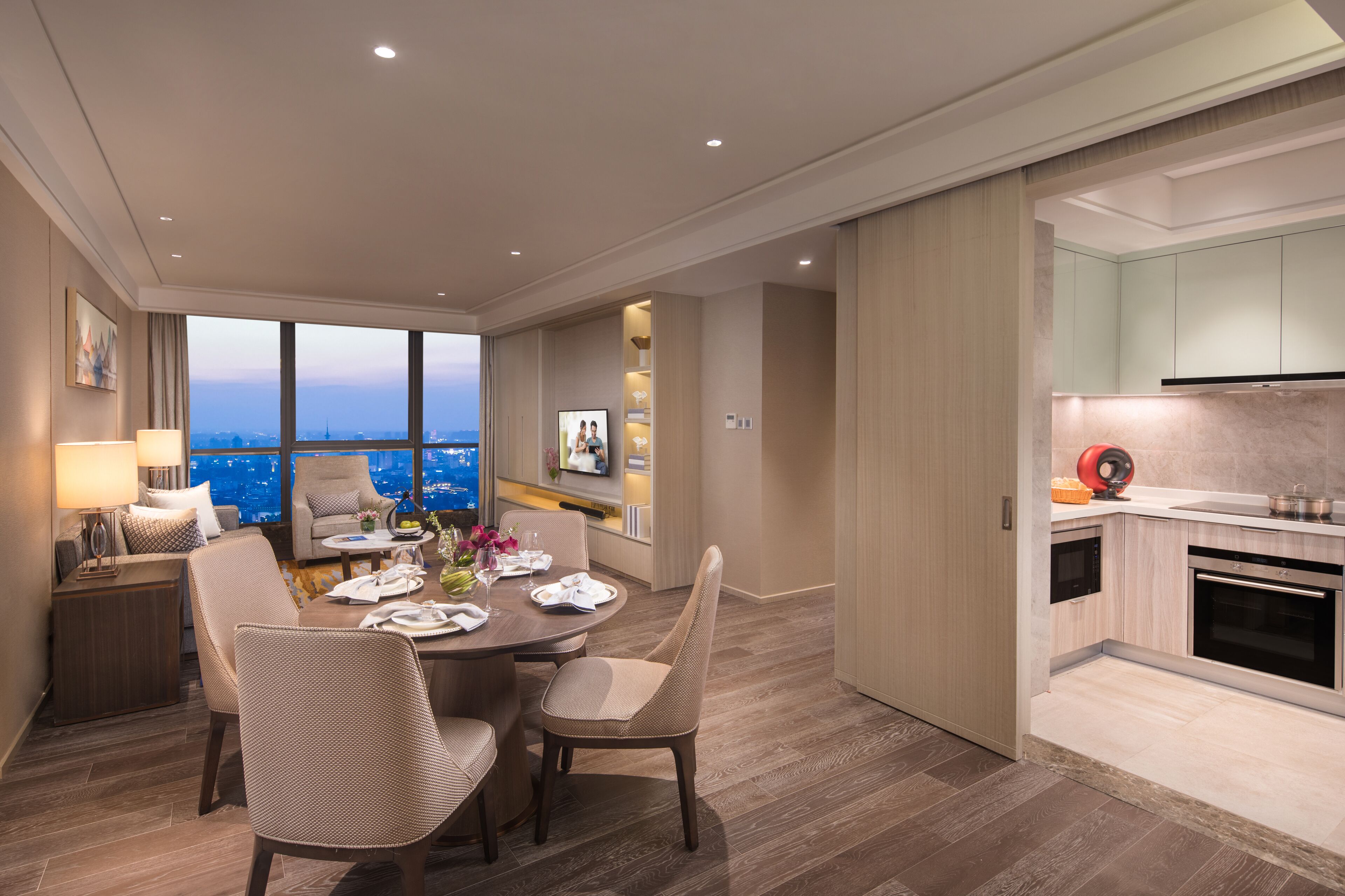 Una habitación de hotel moderna con zona de comedor, cocina y un amplio ventanal con vistas a la ciudad.