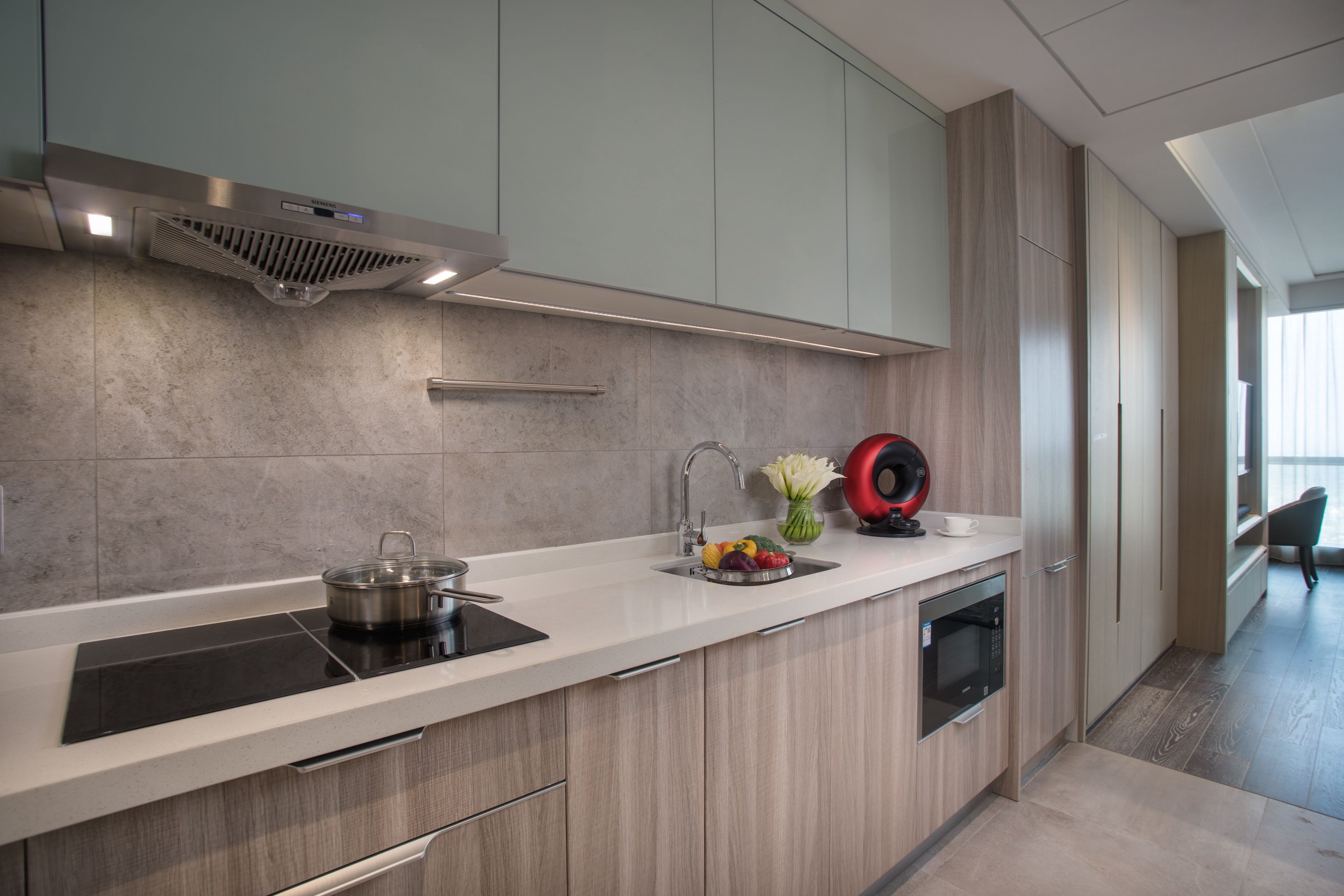 Una cocina moderna con campana extractora de acero inoxidable, horno empotrado y un lavamanos con un jarrón de flores.