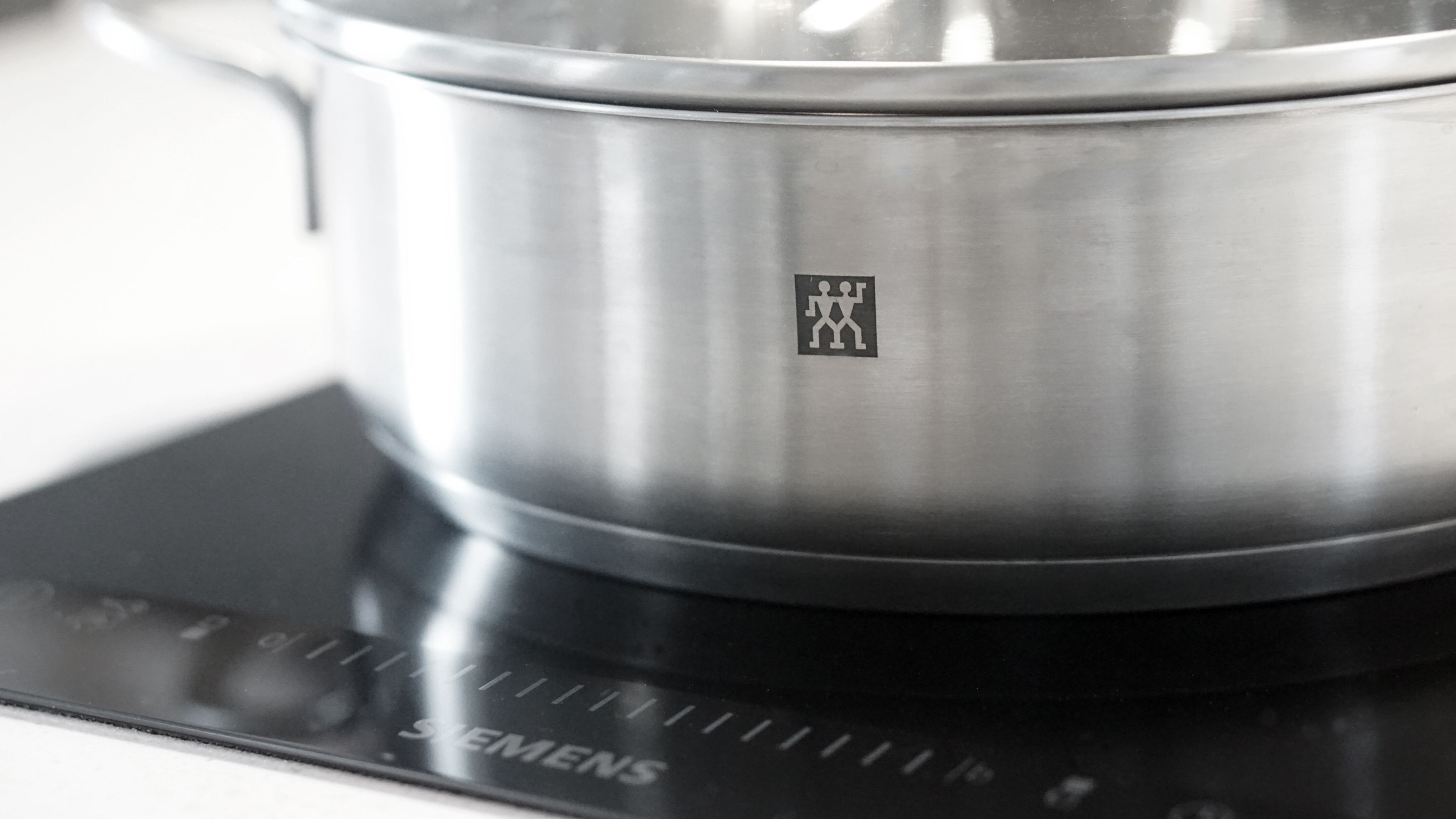A stainless steel pot on a black induction cooktop with the brand name "SIMEENS" visible.