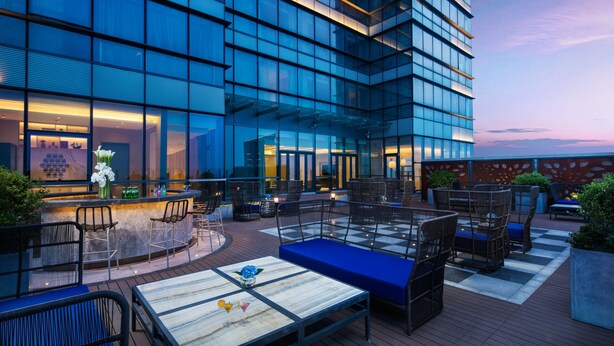 Un área lounge moderna al aire libre con asientos y un bar, con vista a un edificio de vidrio.
