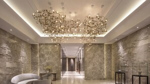Un moderno vestíbulo de hotel con una lámpara de araña geométrica, paredes de mármol y mobiliario contemporáneo.