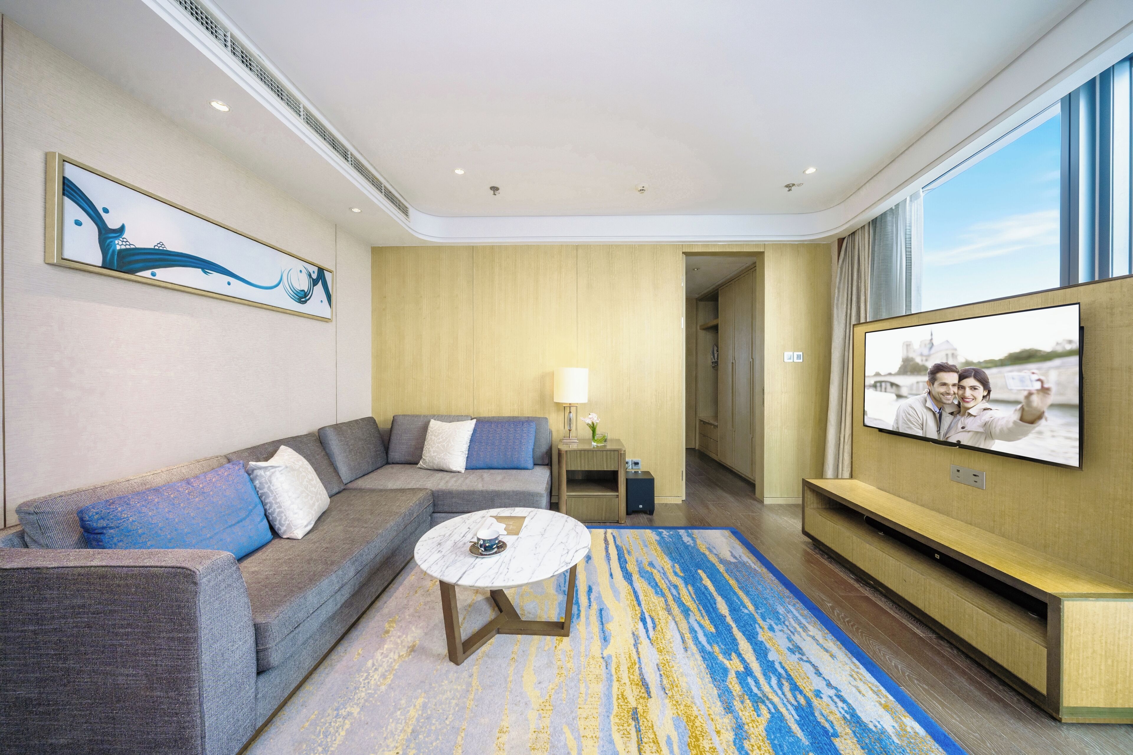 A modern hotel room with a sofa, a coffee table, a TV, and a painting on the wall.