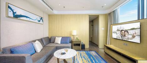 A modern hotel room with a sofa, a coffee table, a TV, and a painting on the wall.