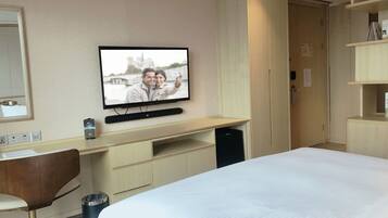 Una habitación de hotel con cama, escritorio con computadora, silla, televisor montado en la pared y un cesto de basura.