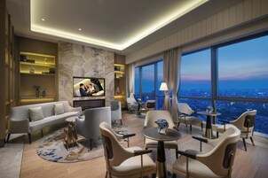 Un salón moderno con sofá, sillas, televisor y vista a la ciudad.