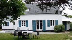 Un edificio blanco con contraventanas azules, una mesa redonda y cuatro sillas en el jardín delantero.