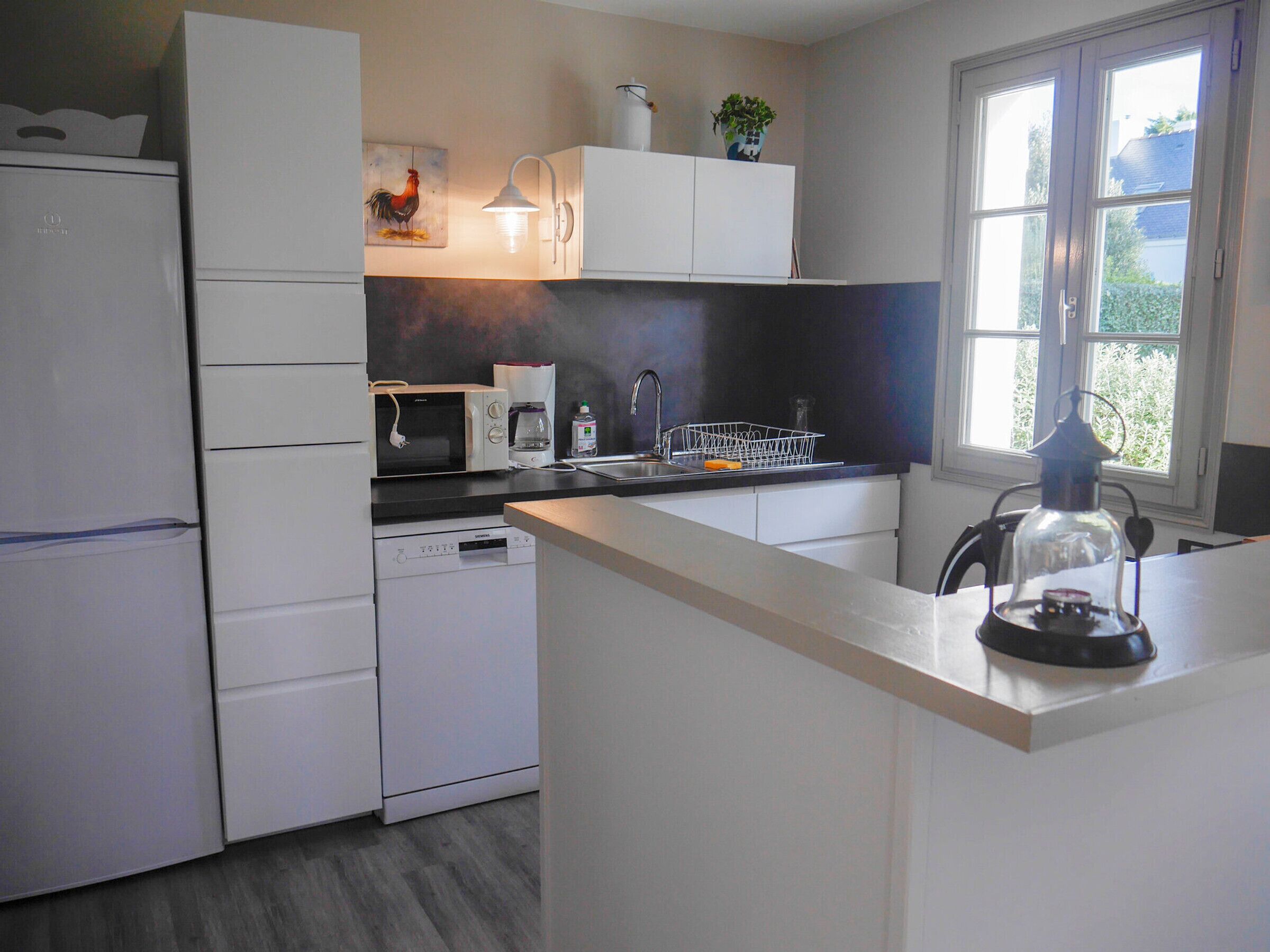 Una cocina moderna con armarios blancos, microondas, cafetera y pileta.