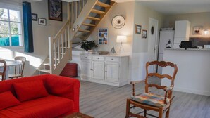 Una sala de estar con un sofá rojo, un sillón de madera y una mesa de centro de madera con revistas. Una escalera conduce a otro nivel.