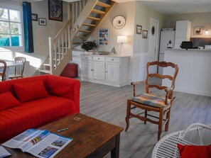 A living room with a red sofa, wooden armchair, and a wooden coffee table with magazines. A staircase leads to another level.