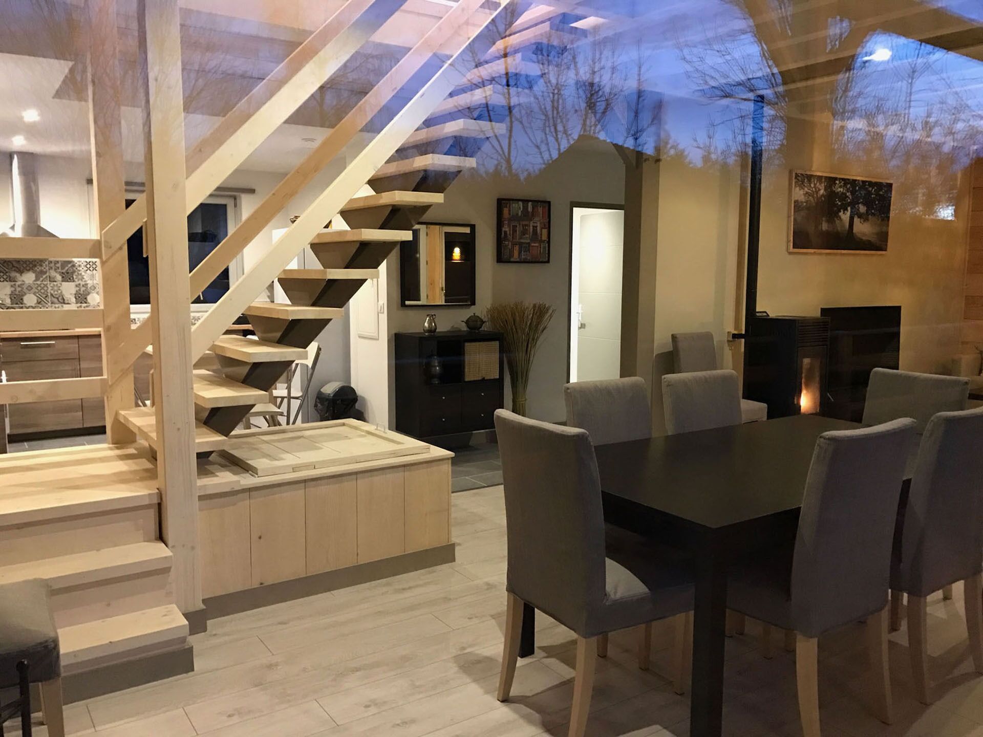 Un intérieur moderne avec un escalier en bois, un coin repas avec des chaises et une cheminée.