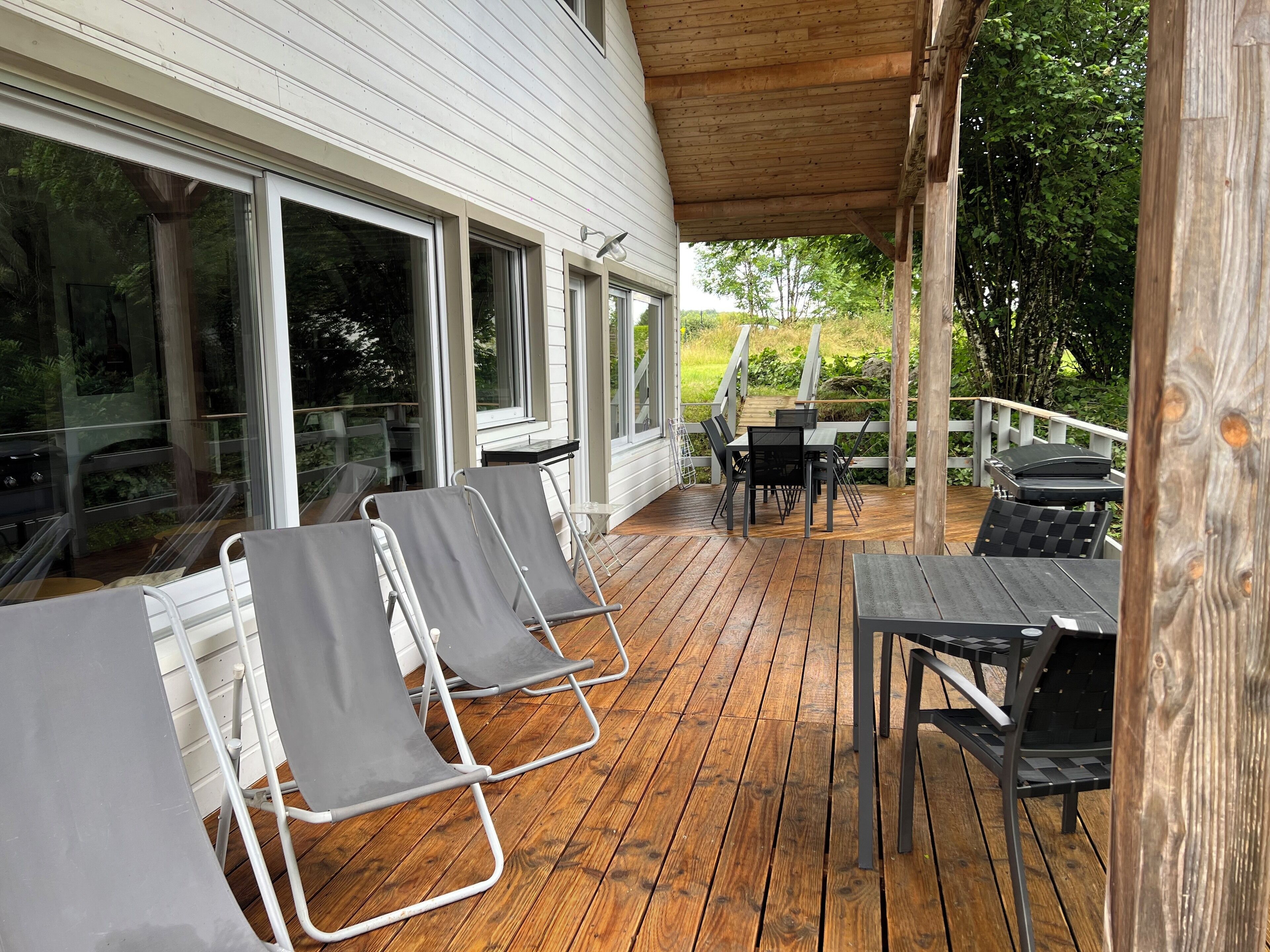 A covered outdoor deck with lounge chairs and a table, surrounded by glass doors and windows.
