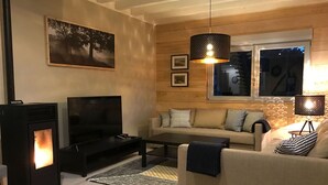 Un salon chaleureux avec une cheminée, un canapé, un téléviseur et une fenêtre donnant sur le ciel nocturne.