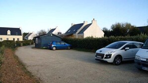 Une allée de gravier mène à un petit bâtiment, près duquel est garée une voiture bleue.