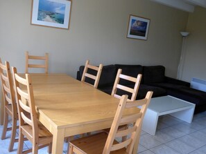 A dining area with a wooden table and chairs, a black sofa, and a white coffee table. - Semi-detached house with garden, 4 beds, peaceful in Locmaria (Locmaria)