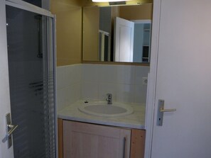 Een badkamer met een douchecabine van glas, een wastafel met spiegel erboven en houten kastjes.