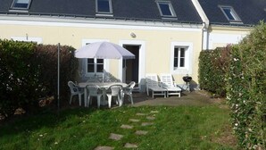 Une maison dotée d’un patio comprenant une table et des chaises, un barbecue et un espace salon couvert avec un parasol.