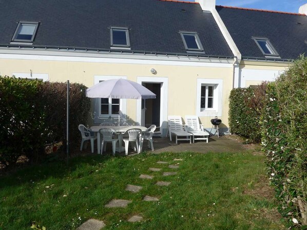 Een huis met een patio, compleet met een tafel en stoelen, een barbecue en een overdekt zitgedeelte met een parasol.