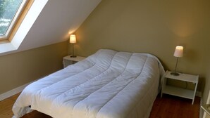 Une chambre avec un lit simple, un plafond en pente, un plancher en bois et deux tables de chevet avec des lampes.