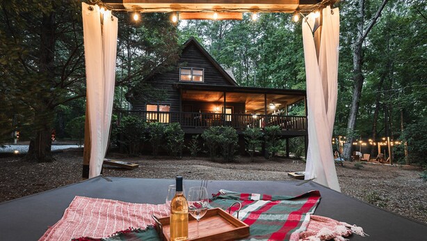 Un espacio al aire libre acogedor con una mesa de madera dispuesta para dos personas, una botella de vino y copas.