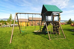 Ein Spielplatz mit Schaukel und Klettergerüst, umgeben von einer Rasenfläche und Wohnhäusern im Hintergrund.