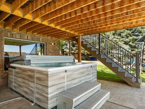 A hot tub in a covered outdoor area with a wooden ceiling and a staircase leading to a deck.
