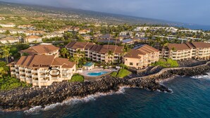 An aerial view of a coastal resort with multiple buildings, a swimming pool, and a rocky shoreline. - Direct oceanfront condo with A/C @ Sea Village (Kailua-Kona)