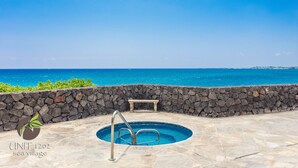 A stone pool with a metal ladder, surrounded by a stone wall, overlooking a clear blue sea. - Direct oceanfront condo with A/C @ Sea Village (Kailua-Kona)
