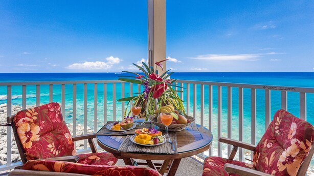 A balcony with a table set for breakfast, overlooking a clear blue sea. - Direct oceanfront condo with A/C @ Sea Village (Kailua-Kona)