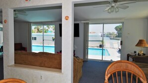 Habitación con vista a una piscina, ventilador de techo y ventana con paisaje playero.