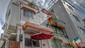 A two-story building with a balcony, a small outdoor seating area with a table and chairs, and potted plants. - La Passione Boutique B&B (Naha)