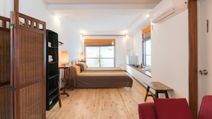 A compact bedroom with a bed, a bedside table, a lamp, a wardrobe, and a window with a view. - La Passione Boutique B&B (Naha)