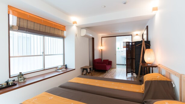 A hotel room with a large bed, a window with blinds, a red chair, and a lamp. - La Passione Boutique B&B (Naha)