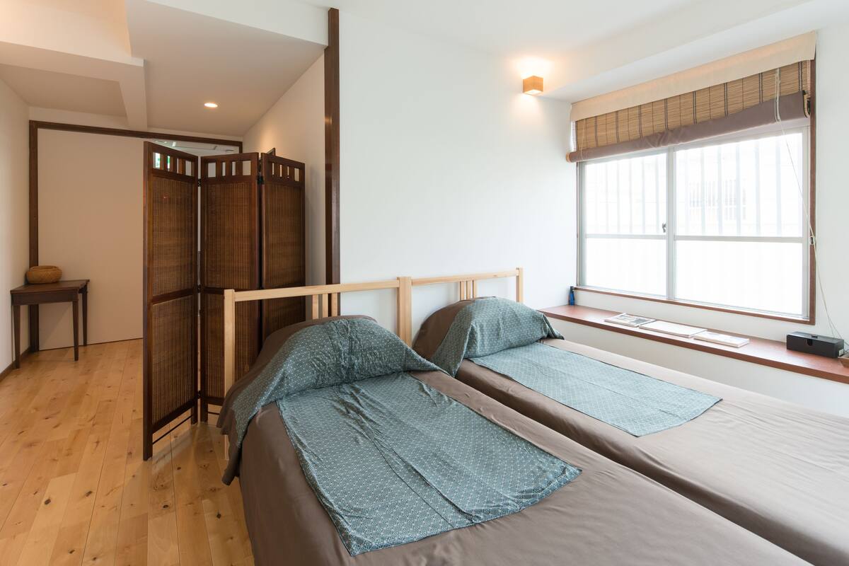 Een kamer met twee bedden, een houten vloer, een raam met uitzicht en een traditionele Japanse schuifdeur.