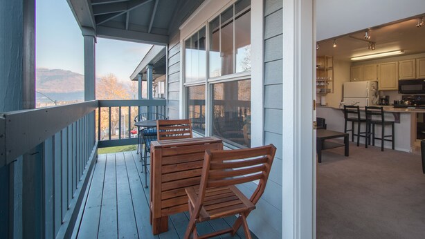Eine überdachte Veranda mit Holzmöbeln, Blick auf die Berge und einer Küchenzeile mit Holdekor und Kühlschrank.