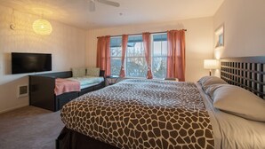 Ein Schlafzimmer mit einem großen Bett, einem Fernseher, einem Deckenventilator und einem Fenster mit Vorhängen.