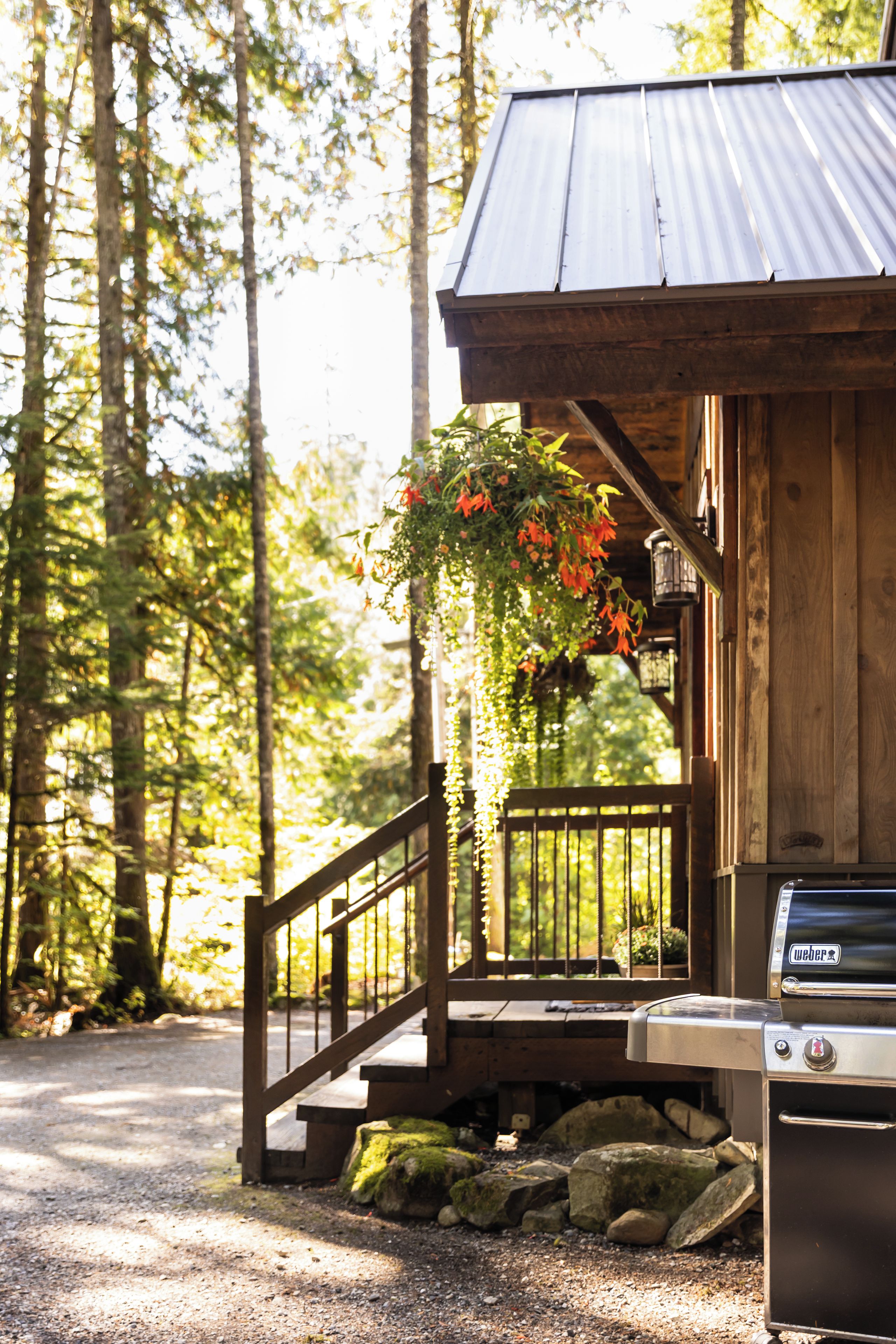 A wooden cabin with a porch, a grill, and a hanging flower basket.