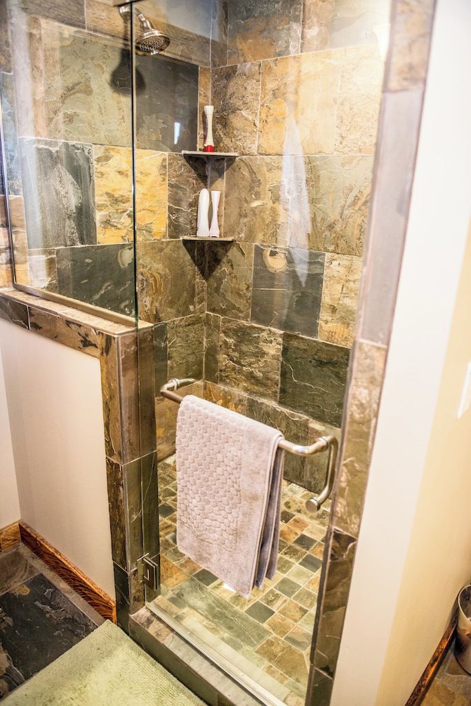 A glass-enclosed shower with a marble wall, a towel rack, and a shelf with toiletries.