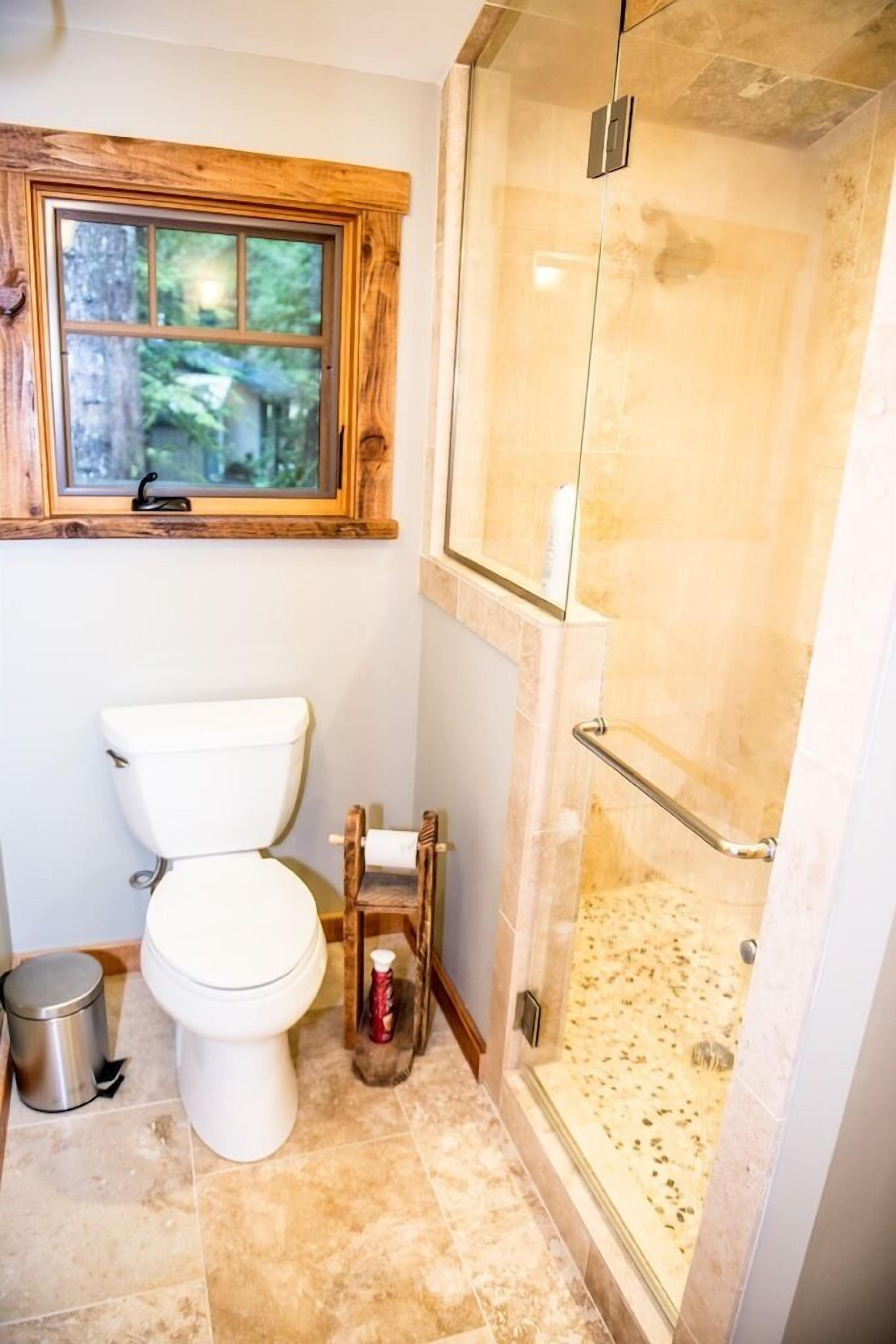 Une salle de bain comprenant des toilettes, une douche avec une porte en verre et une fenêtre située au-dessus des toilettes.