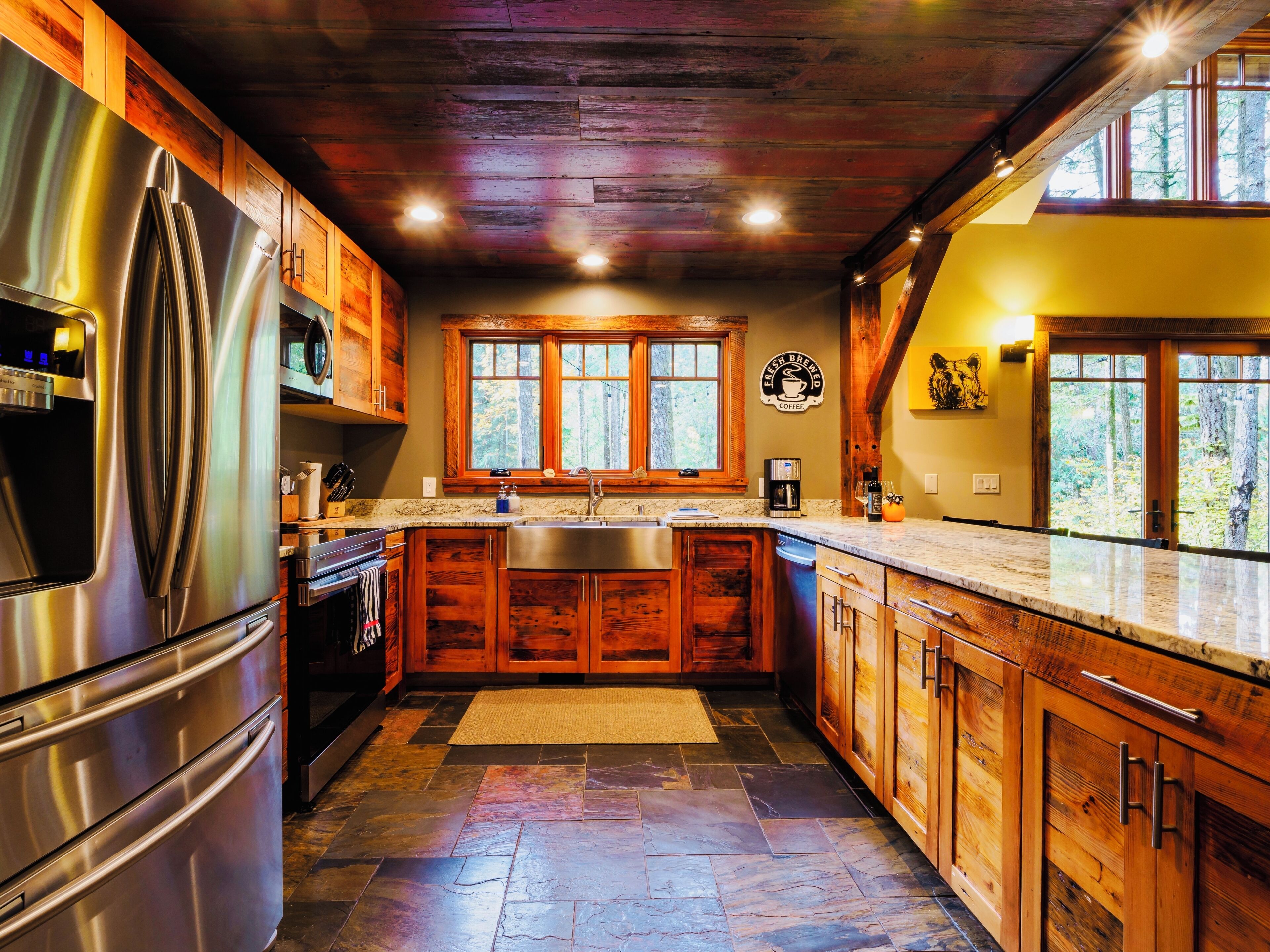 A modern kitchen with wooden cabinets, a stainless steel refrigerator, and a large window providing a view of the outdoors.