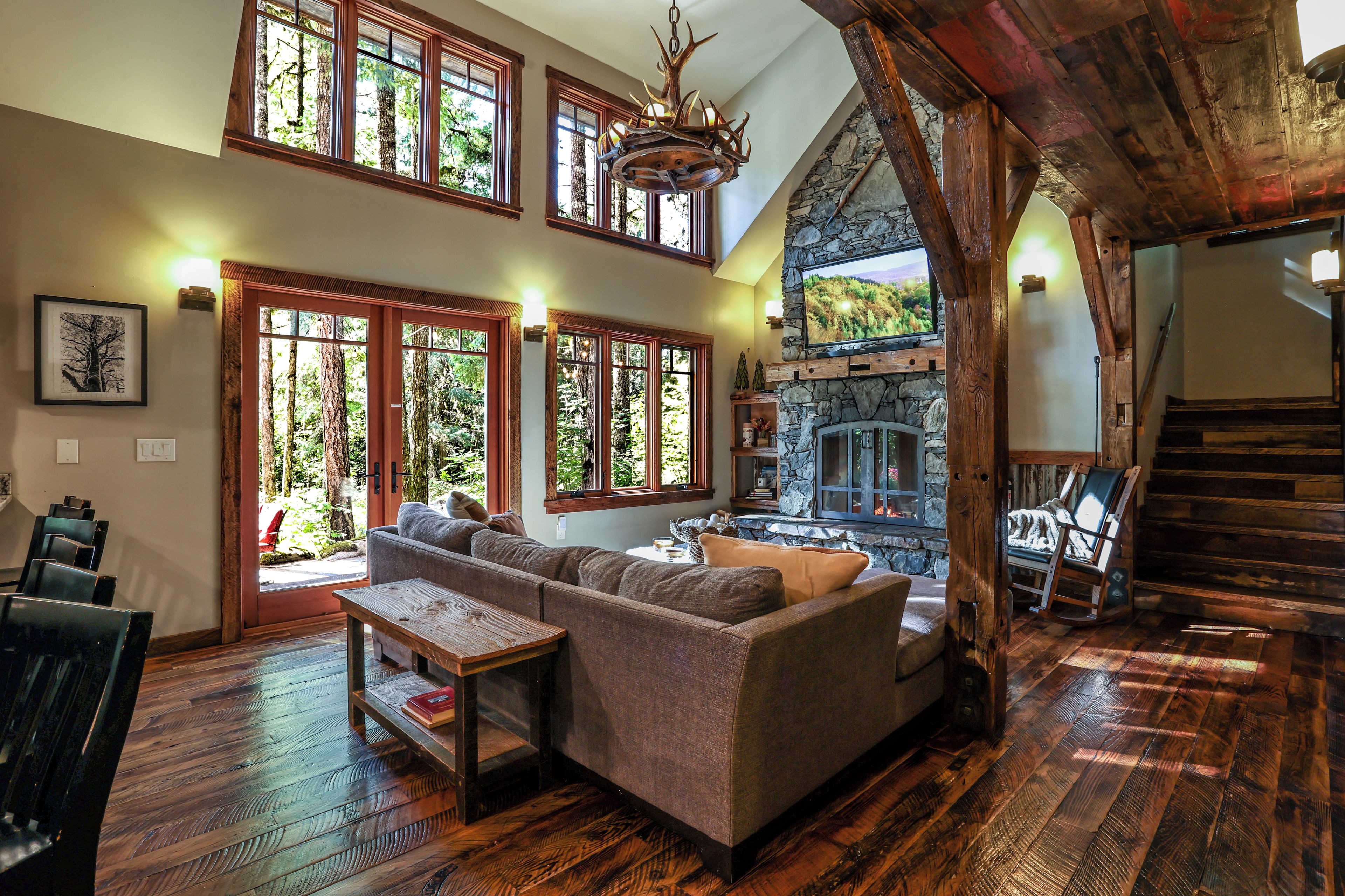 A spacious living area with a large sofa, a wooden coffee table, and a stone fireplace. There are multiple windows allowing natural light and views of the outdoors.