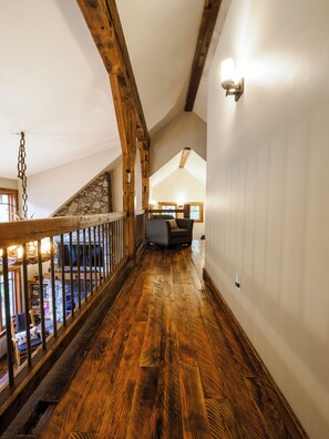 A wooden staircase leading to a loft area with a stone wall and a view of the living room below.