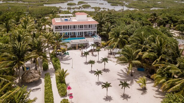 Een resort met een zwembad, omgeven door palmbomen en een strand.