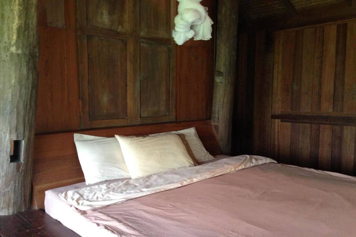 Uma cama de madeira com cabeceira, almofadas brancas e colcha rosa.