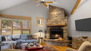 A cozy living room with a stone fireplace, a large window, and a flat-screen TV. - Outpost: Moose Creek 20 - Private Hot Tub! (Teton Village)